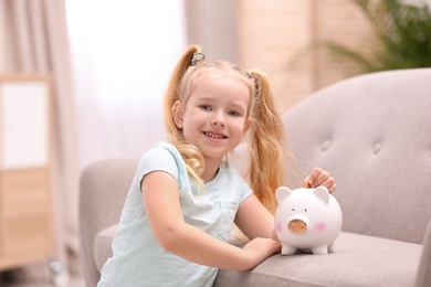 Photo of Little girl with piggy bank and money at home