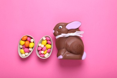Photo of Chocolate Easter bunny, halves of egg and candies on pink background, flat lay