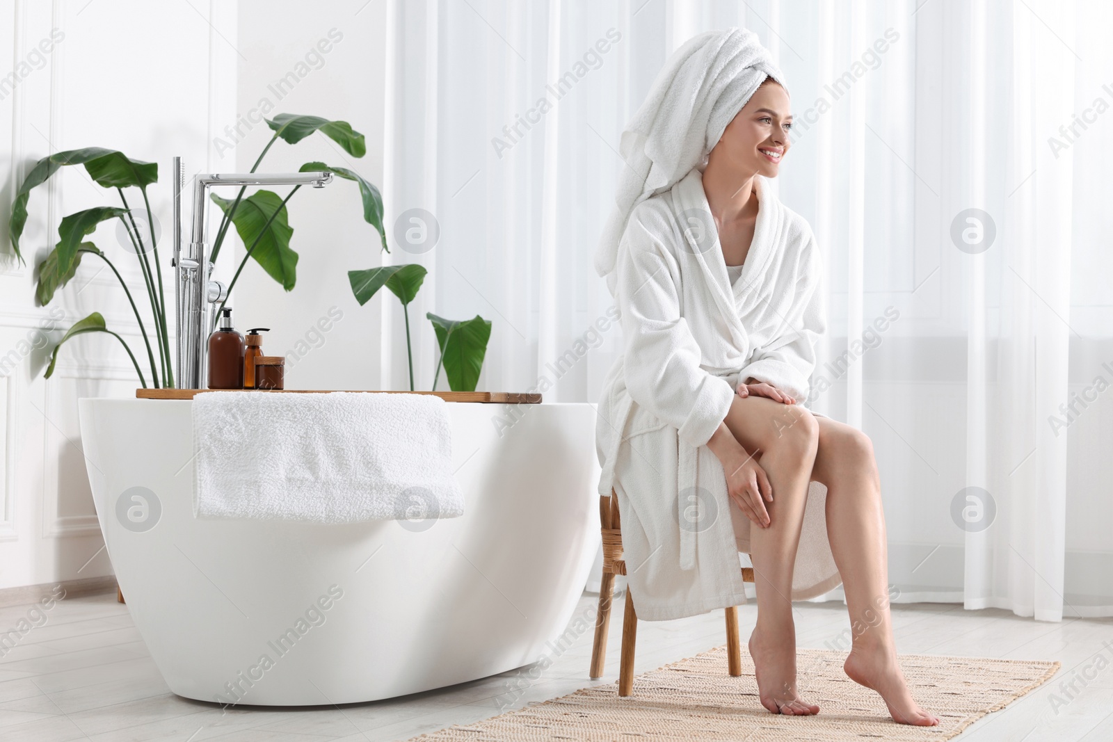 Photo of Beautiful young woman touching her smooth legs in bathroom, space for text