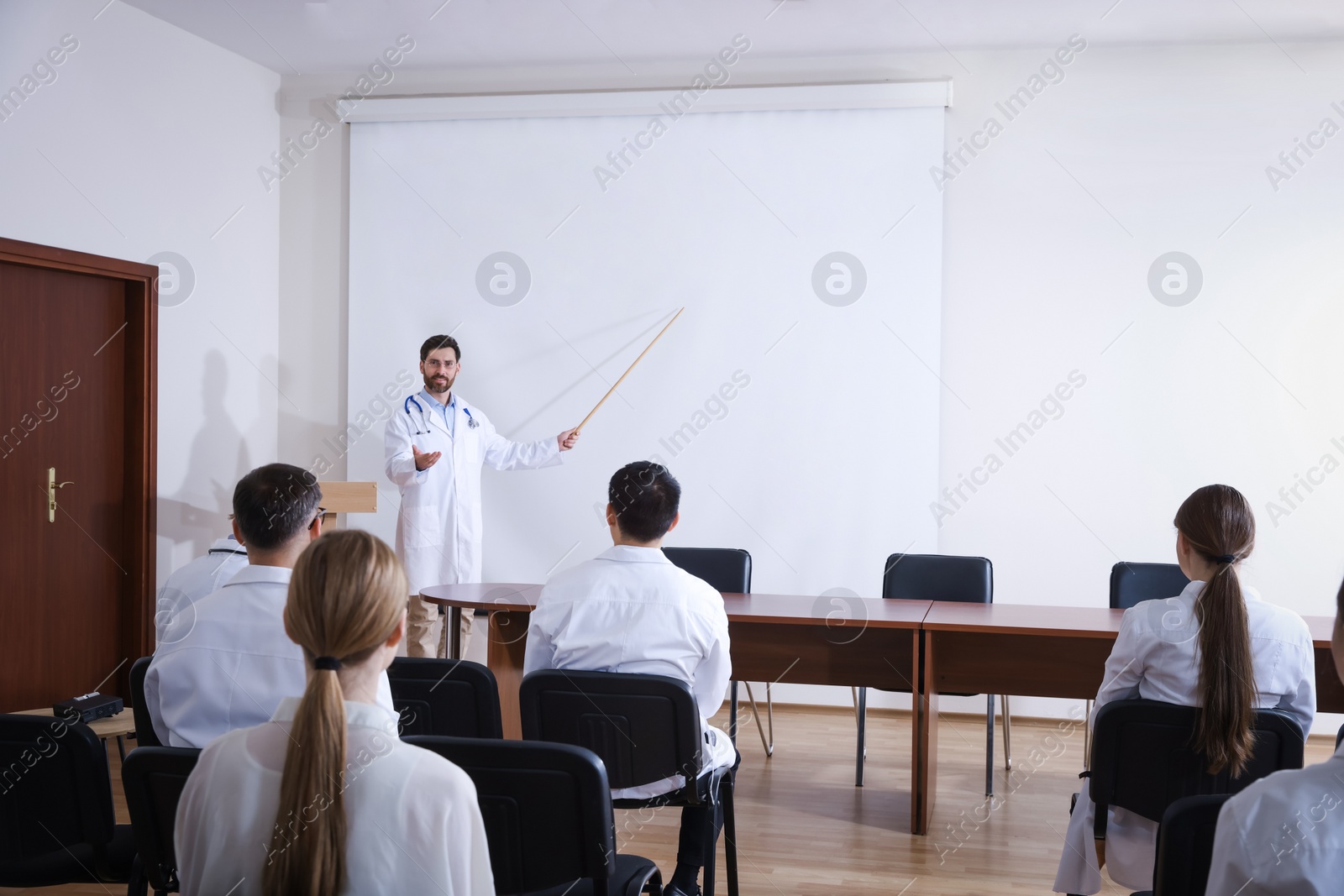 Photo of Doctor giving lecture in conference room with projection screen