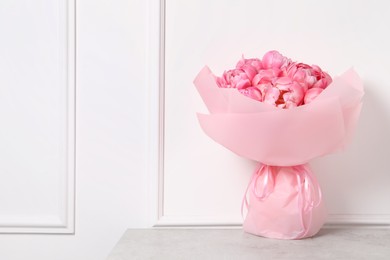 Photo of Bouquet of beautiful pink peonies on table near white wall. Space for text
