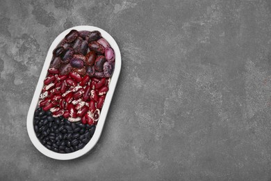 Photo of Plate with different types of beans on grey table, top view. Space for text