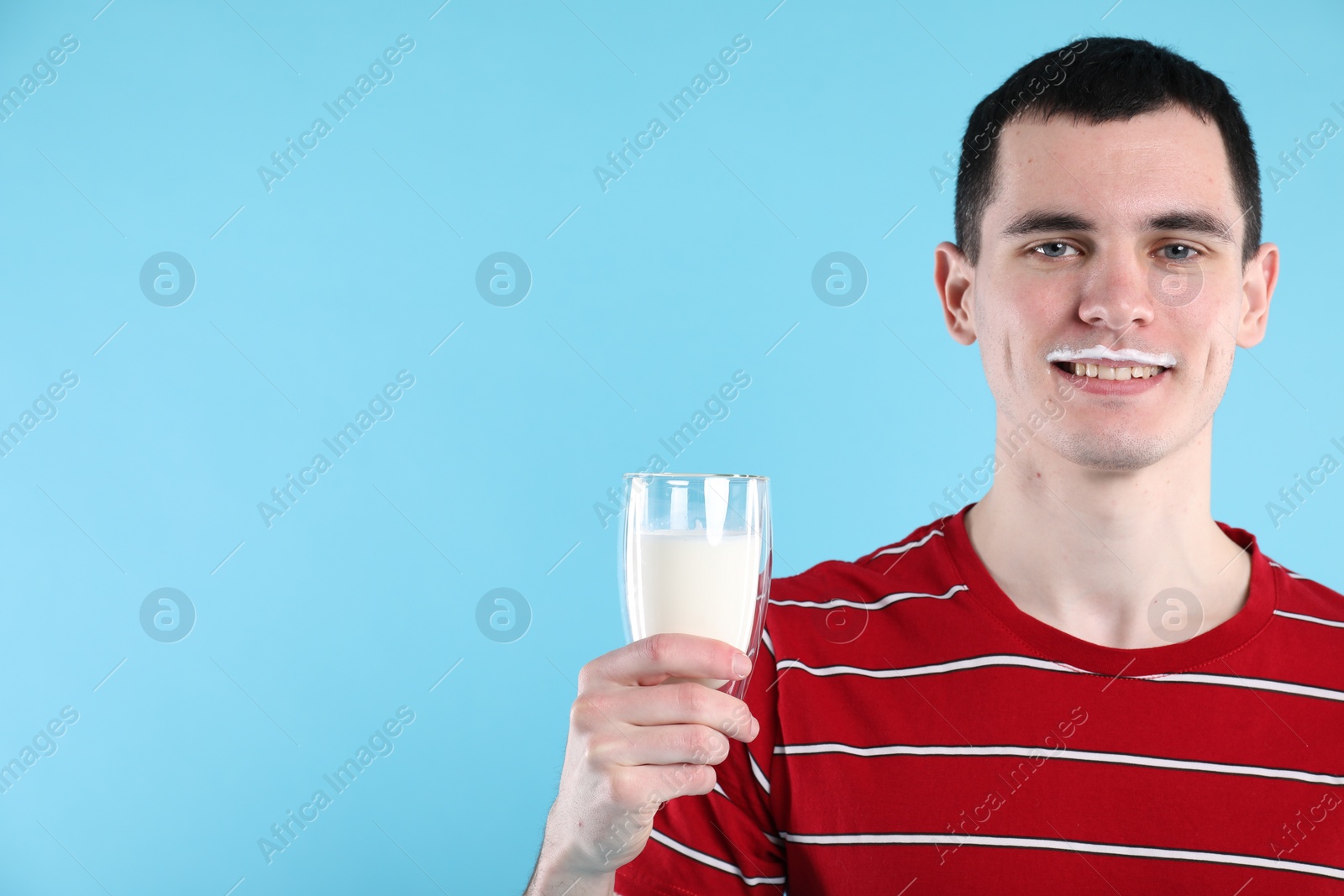 Photo of Happy man with milk mustache holding glass of tasty dairy drink on light blue background, space for text