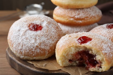 Photo of Delicious donuts with jelly and powdered sugar on wooden board, closeup