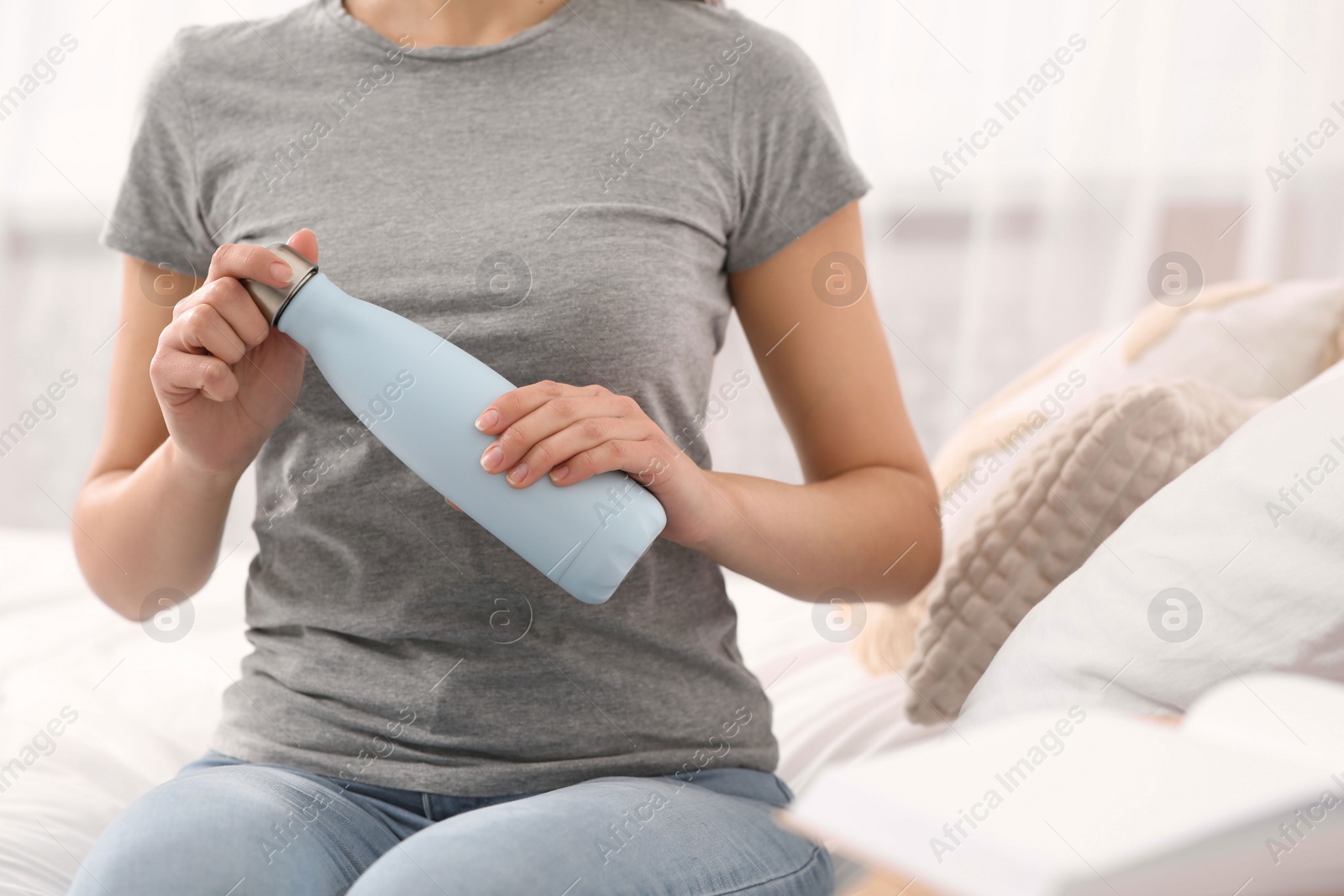 Photo of Woman holding thermo bottle on bed at home, closeup. Space for text