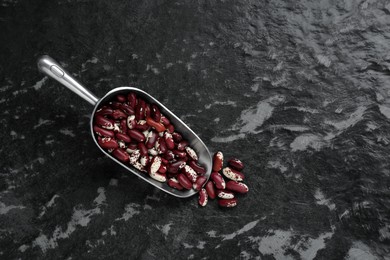 Photo of Metal scoop with dry kidney beans on black textured table, flat lay. Space for text
