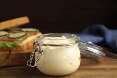 Photo of Jar of delicious mayonnaise near fresh sandwich on wooden table