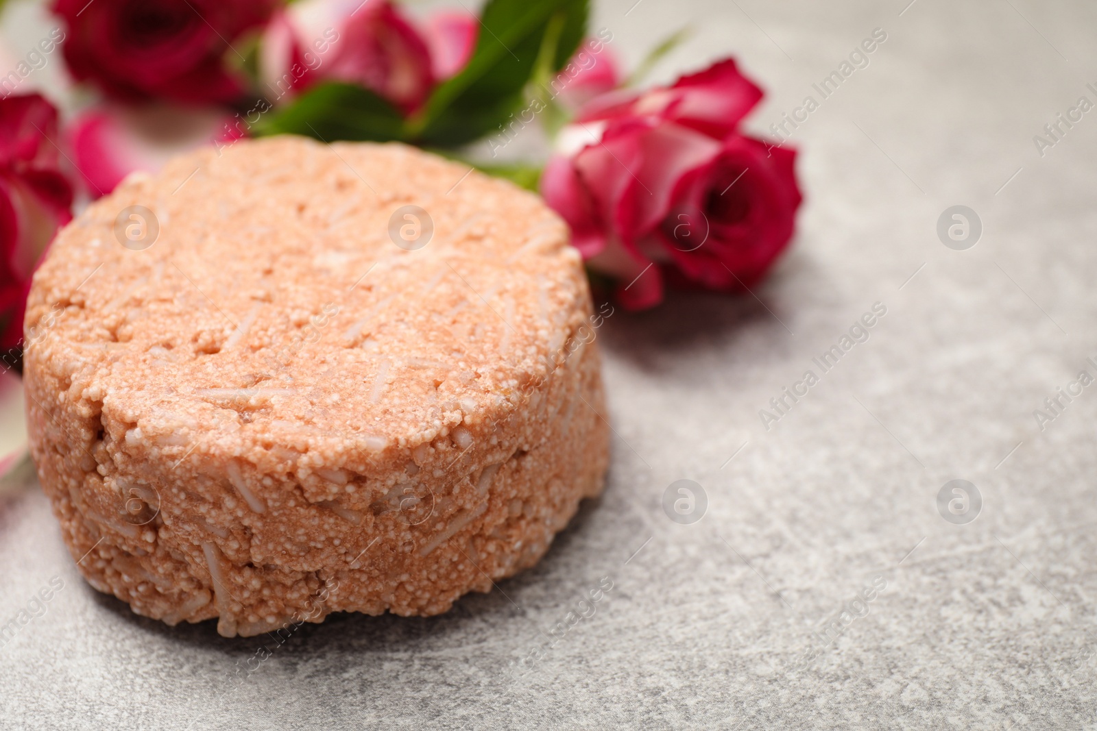 Photo of Solid shampoo bar and roses on light grey table, closeup. Space for text