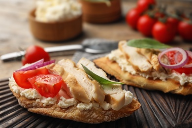 Photo of Board with delicious chicken bruschettas on table, closeup