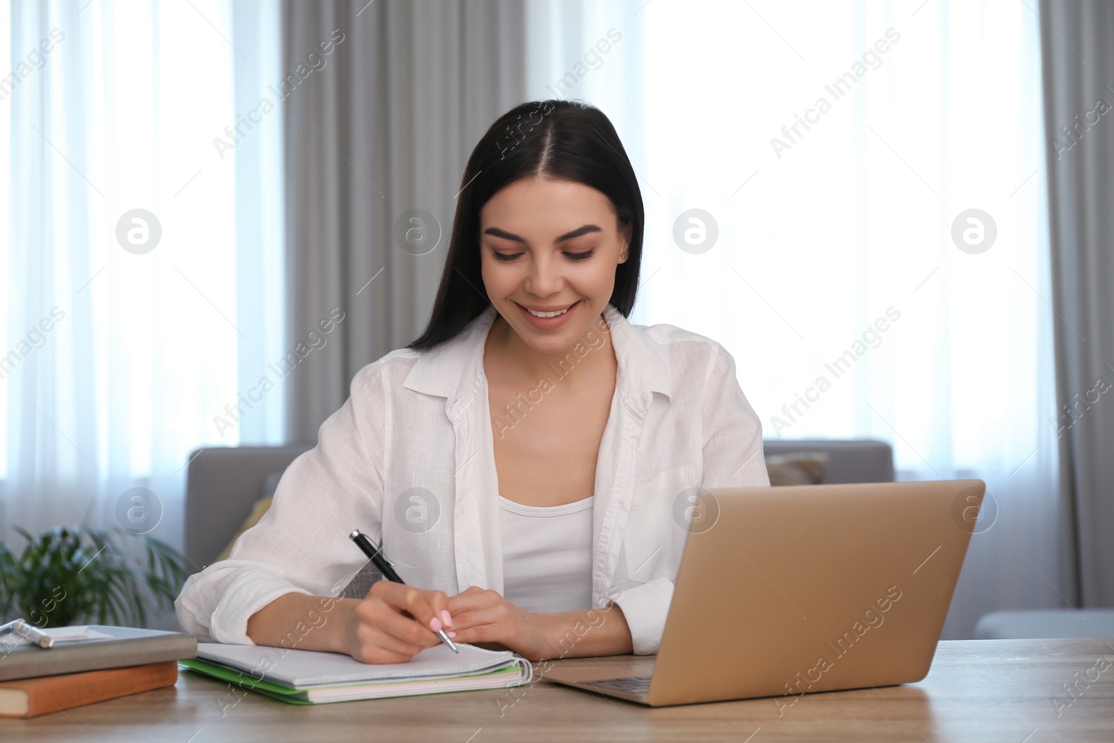 Photo of Young woman taking notes during online webinar at table indoors