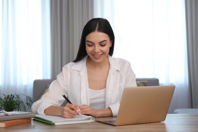 Photo of Young woman taking notes during online webinar at table indoors
