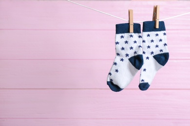 Photo of Pair of socks on laundry line against pink wooden background, space for text. Baby accessories