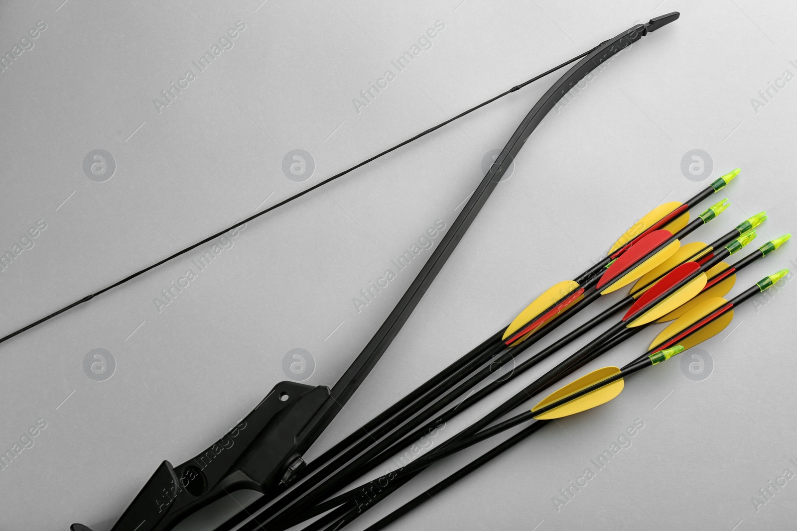 Photo of Black bow and set of arrows on light grey background, flat lay. Archery sports equipment