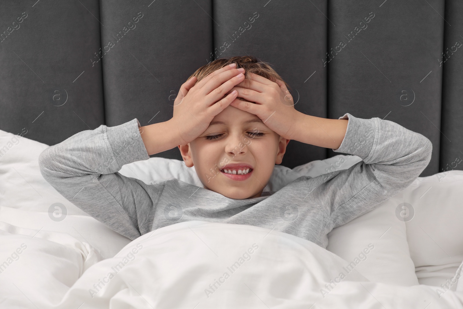 Photo of Little boy suffering from headache in bed at home