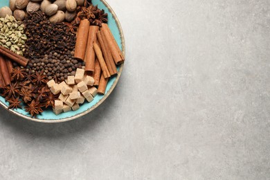 Photo of Different spices and nuts in bowl on light gray textured table, top view. Space for text