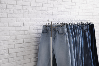 Rack with stylish jeans near brick wall