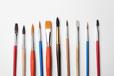 Different paint brushes on white background, top view