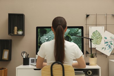Photo of Woman sitting at white desk with computer near beige wall, back view. Interior design