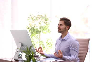 Photo of Young businessman meditating at workplace. Zen concept