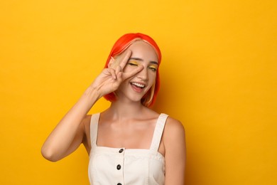 Beautiful young woman with bright dyed hair on orange background