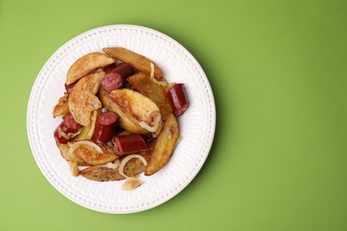 Photo of Delicious baked potato with thin dry smoked sausages and onion on green table, top view. Space for text