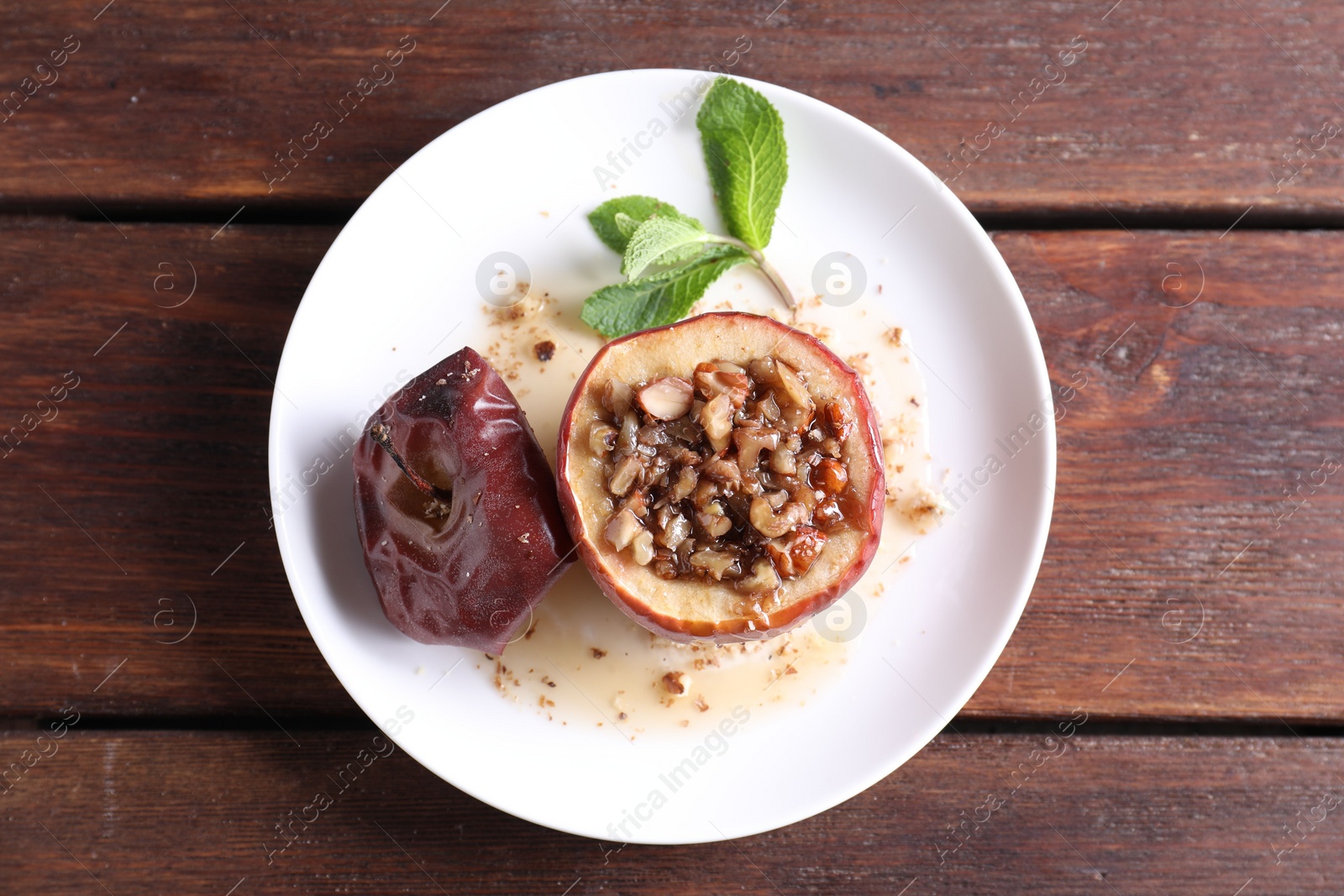 Photo of Tasty baked apple with nuts, honey and mint on wooden table, top view