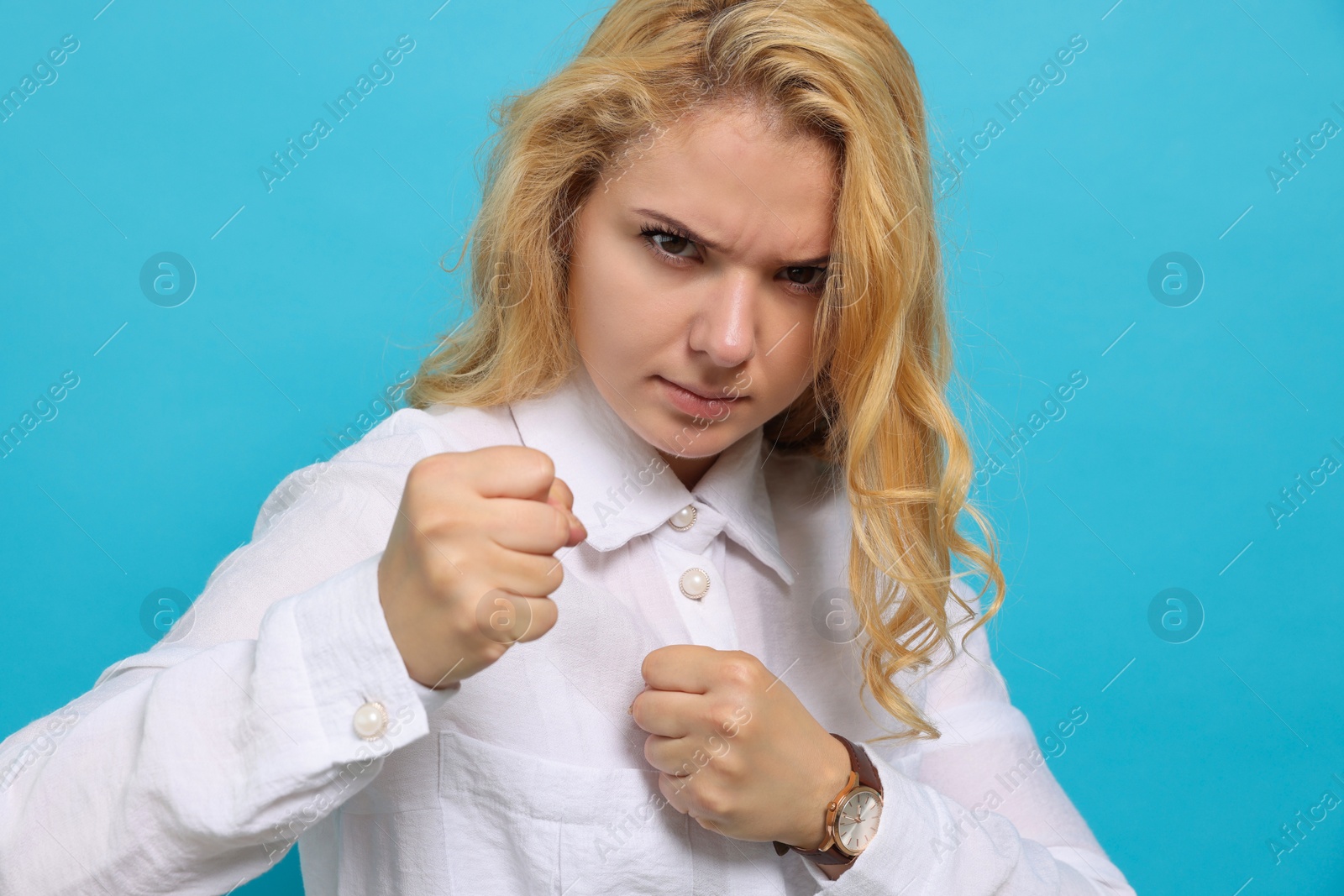 Photo of Angry young woman ready to fight on light blue background