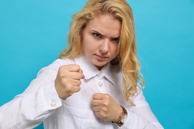 Photo of Angry young woman ready to fight on light blue background