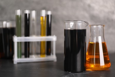 Photo of Beakers, flask and test tubes with different types of oil on grey textured table, closeup