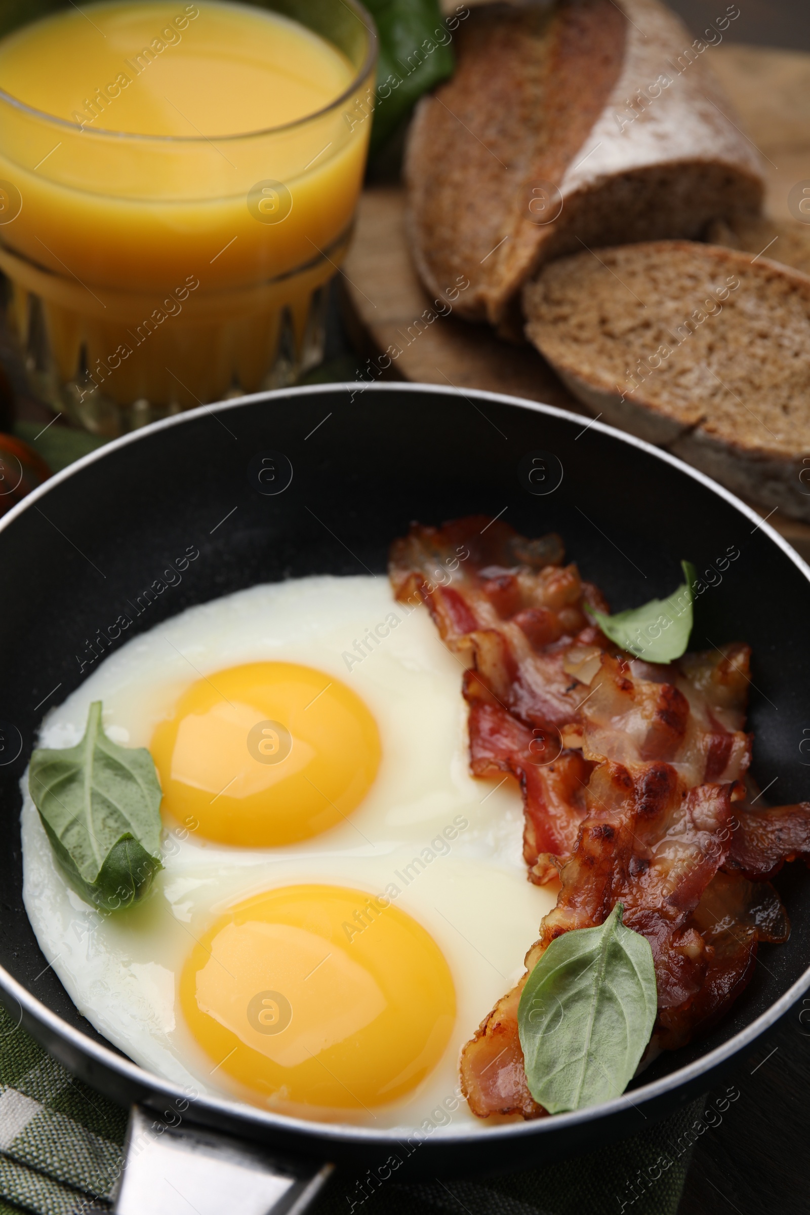 Photo of Fried eggs, bacon, basil, juice and bread on table