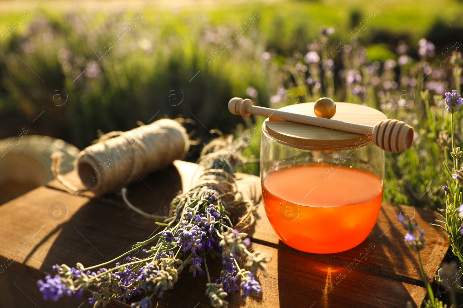 Photo of Jar of honey on wooden table in lavender field