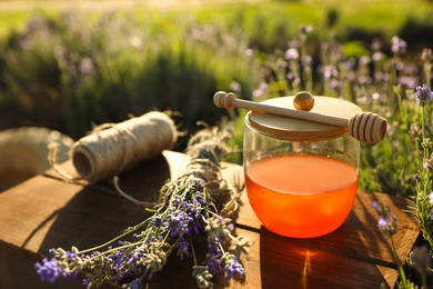 Photo of Jar of honey on wooden table in lavender field