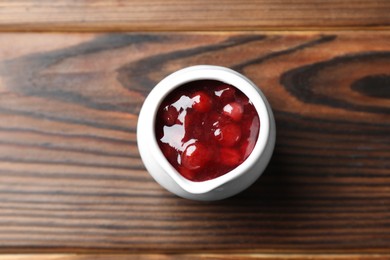 Photo of Fresh cranberry sauce in pitcher on wooden table, top view