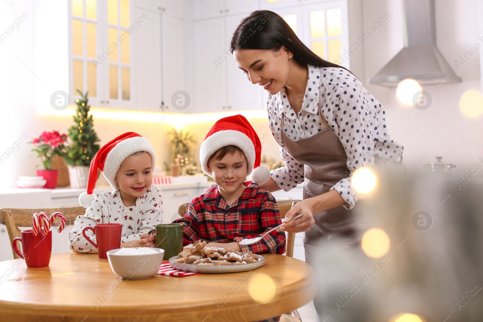 Photo of Mother putting sugar powder onto Christmas cookies for her cute little children in kitchen