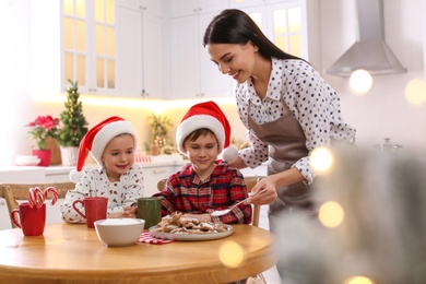 Photo of Mother putting sugar powder onto Christmas cookies for her cute little children in kitchen