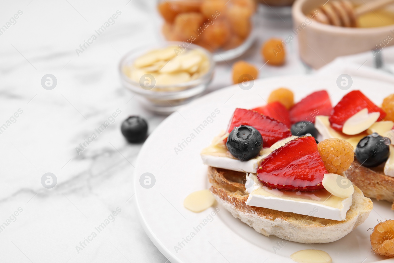 Photo of Tasty sandwiches with brie cheese, fresh berries and almond flakes on white marble table, closeup. Space for text