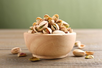 Photo of Tasty pistachios in bowl on wooden table against olive background, closeup