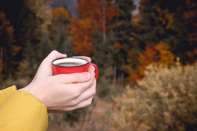 Photo of Young woman with mug of hot instant coffee near forest, closeup