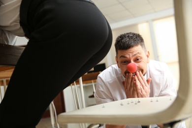 Photo of Man putting pins on chair while his colleague sitting down in office, closeup. Funny joke