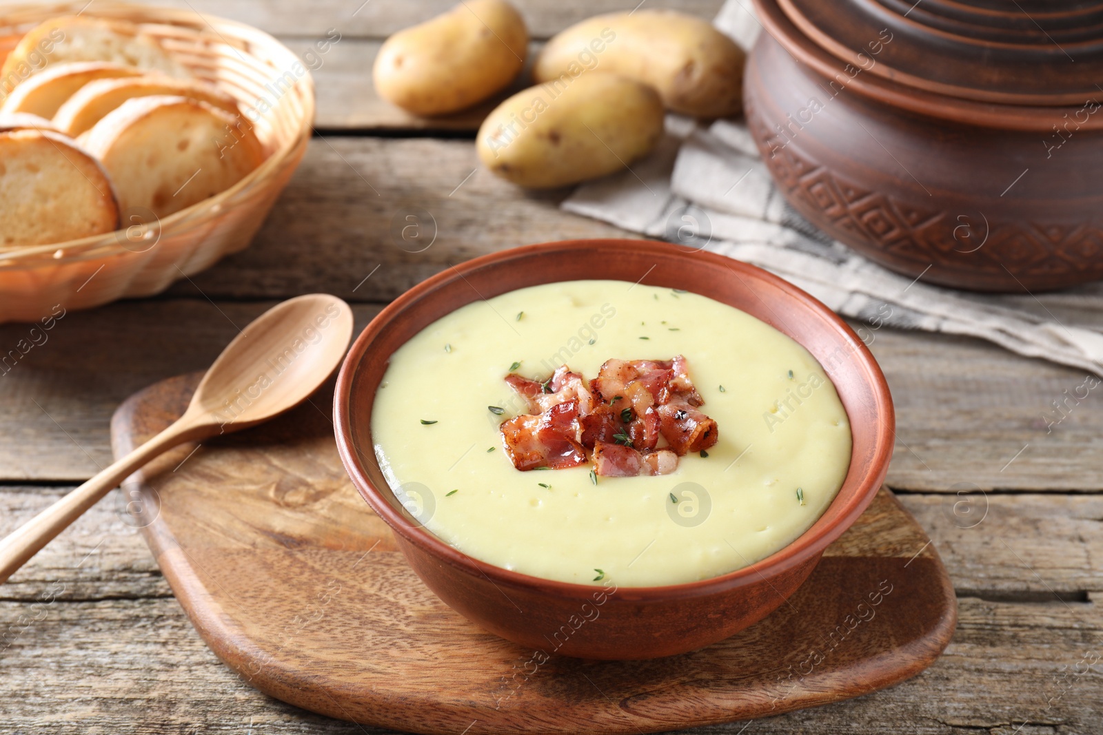 Photo of Tasty potato soup with bacon and rosemary in bowl served on wooden table