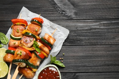 Photo of Delicious chicken shish kebabs with vegetables and ketchup on black wooden table, flat lay. Space for text