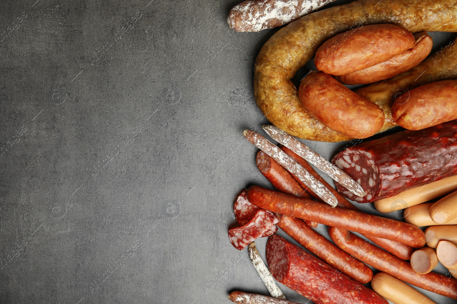 Photo of Different types of sausages on grey background, flat lay. Space for text