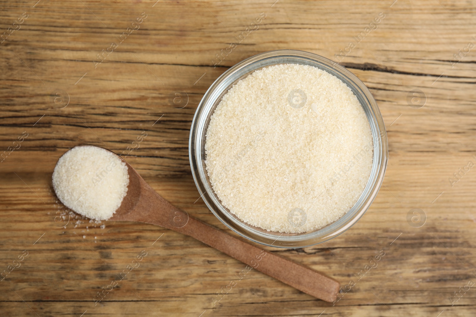 Photo of Gelatin powder in glass bowl and spoon on wooden table, flat lay