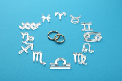 Zodiac signs and wedding rings on light blue background, closeup