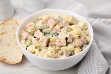 Photo of Tasty Olivier salad with boiled sausage in bowl and bread on white table, closeup