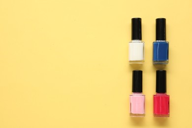 Photo of Bright nail polishes in bottles on yellow background, flat lay. Space for text