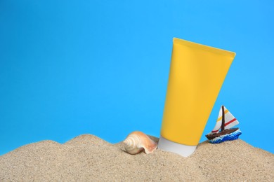 Photo of Sand with sunscreen, seashell and toy sailboat against blue background, space for text. Sun protection care