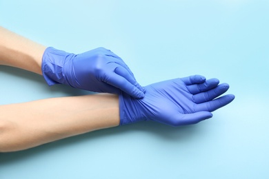 Photo of Person putting on medical gloves against light blue background, closeup of hands