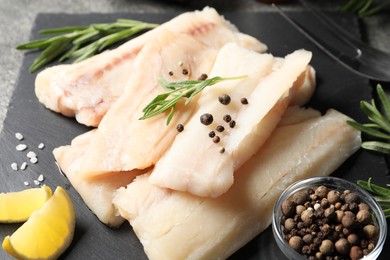 Photo of Pieces of raw cod fish, rosemary, peppercorns and lemon on table, closeup
