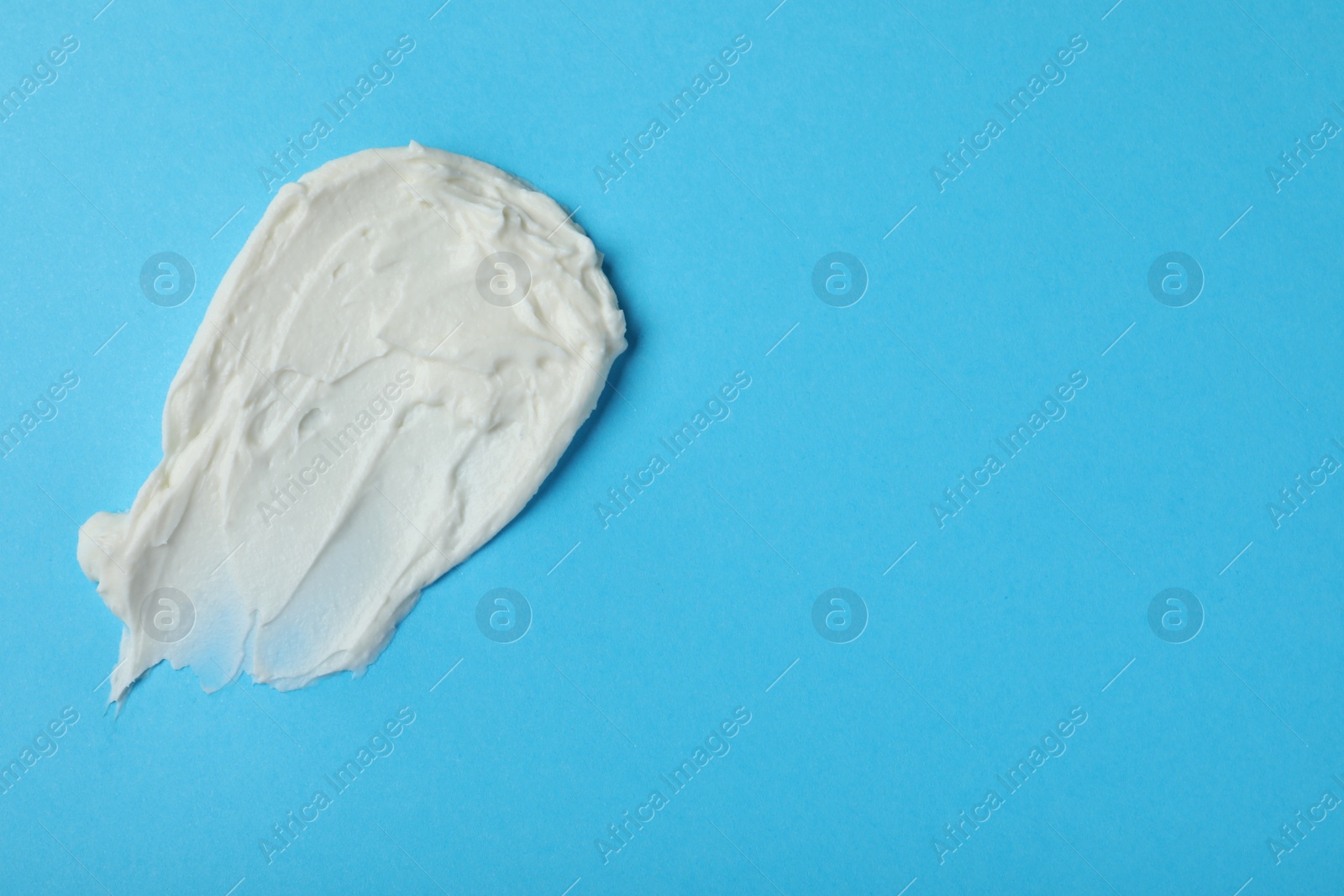 Photo of Smear of delicious cream cheese on light blue background, top view. Space for text